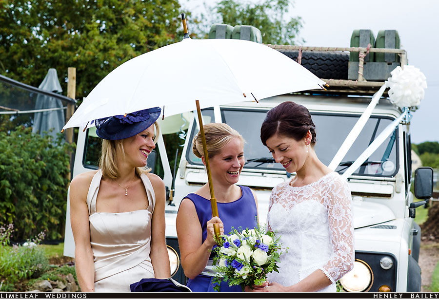 Bride and bridesmaids laugh by her wedding car before the wedding ceremony